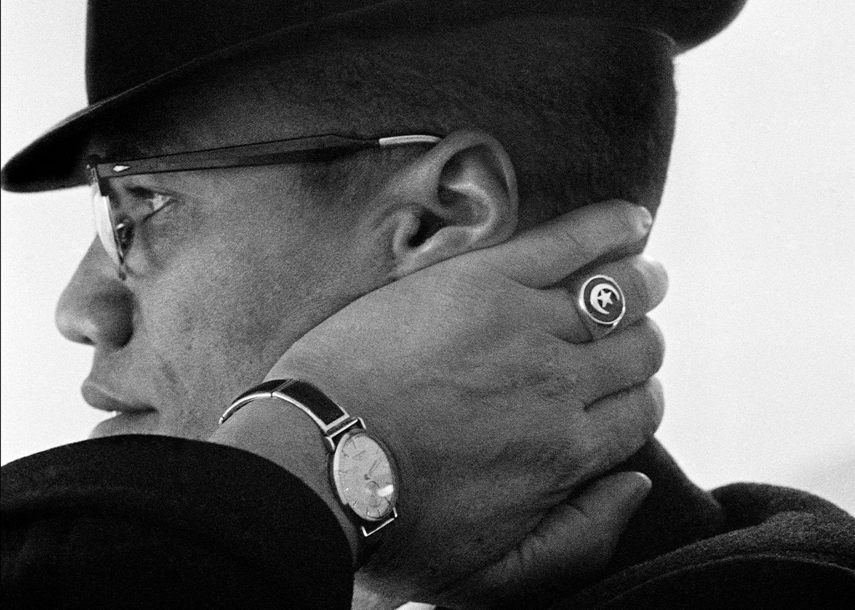 Malcolm X is seen in profile with his hand placed on the back of his neck